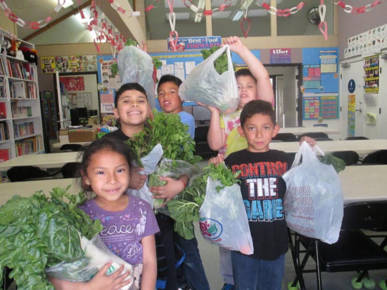 A group of smiling young children hold up bags overflowing with greens donated by Food Forward.