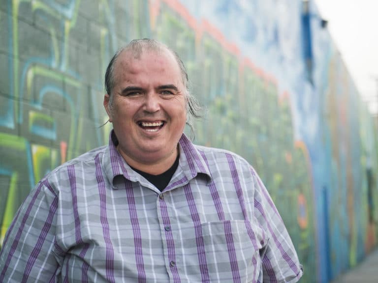 A staff member smiles in front of a wall of graffiti art.