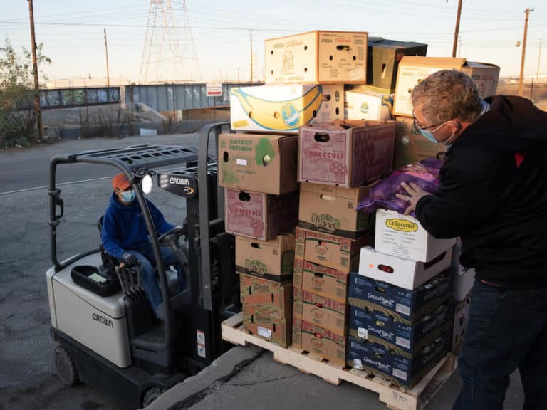 Food Forward staff load a pallet stacked with boxes of produce onto a forklift.