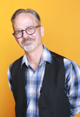Rick smiling in front of orange background